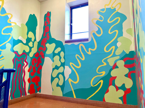 A section of mural in a stairwell with large light blue and dark blue absract shapes on the walls. Breaking up the blue are blobs of red and green, with a yellow wiggly line cutting up the wall.