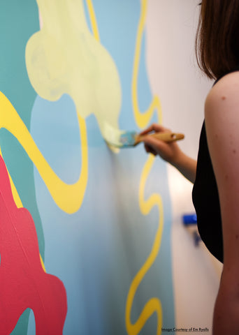 Beth Morgan painting green paint into a wall covered in abstract shapes.