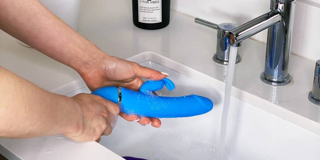 mains de femme qui nettoient un vibromasseur rabbit bleu sous l'eau