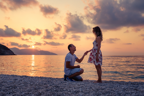 man and woman at the beach, man is kneeling down and holding woman’s hand