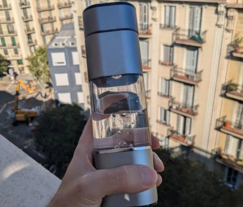 Hand holding clear water bottle with buildings in the background.