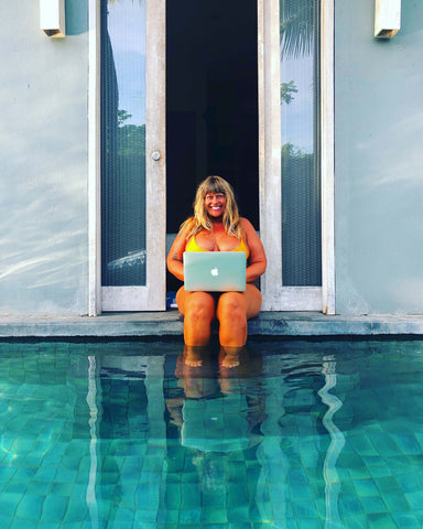 Heather Brown sitting in a blue pool with her laptop on her lap, smiling at the camera.