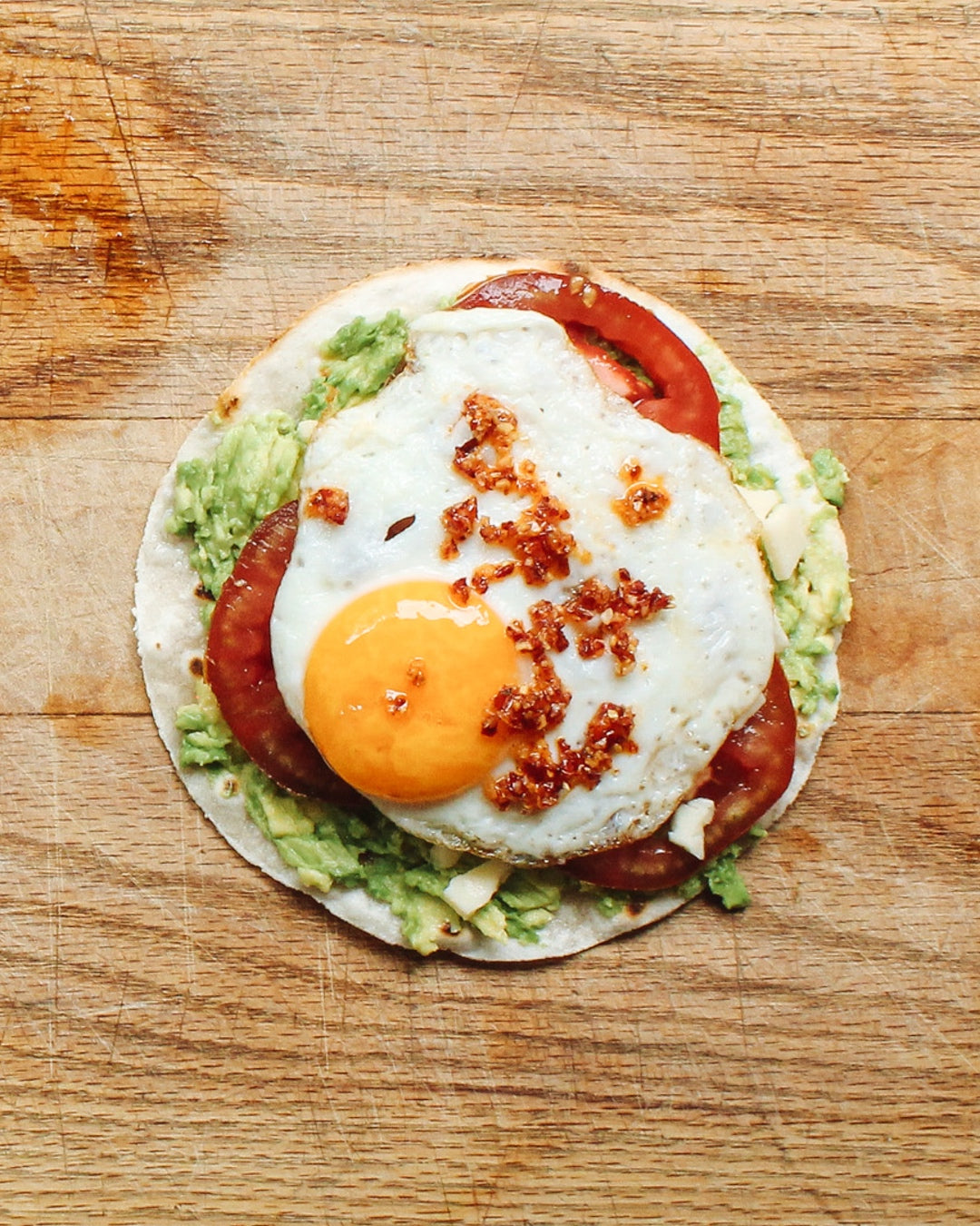 A fully customizable breakfast tostada topped with smashed avocado, chili crunch, melty cheese, and a sunny fried egg. | peteandgerrys.com