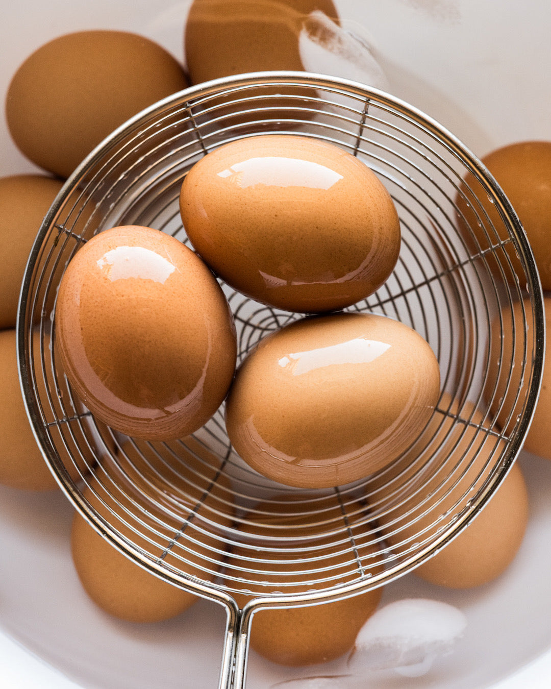A metal strainer lifts perfectly-cooked hard-boiled eggs out of an ice water bath. | peteandgerrys.com