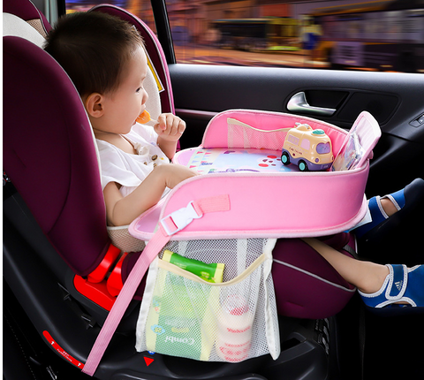 Toddler comfortably seated in a car seat with a pink travel tray, featuring a cup holder and compartments for toys and snacks. The tray provides a sturdy surface for playtime or mealtime, enhancing the in-car experience for young children. Discover this convenient car seat accessory for kids at OnlineFamStore.com, perfect for keeping little ones entertained on the road.