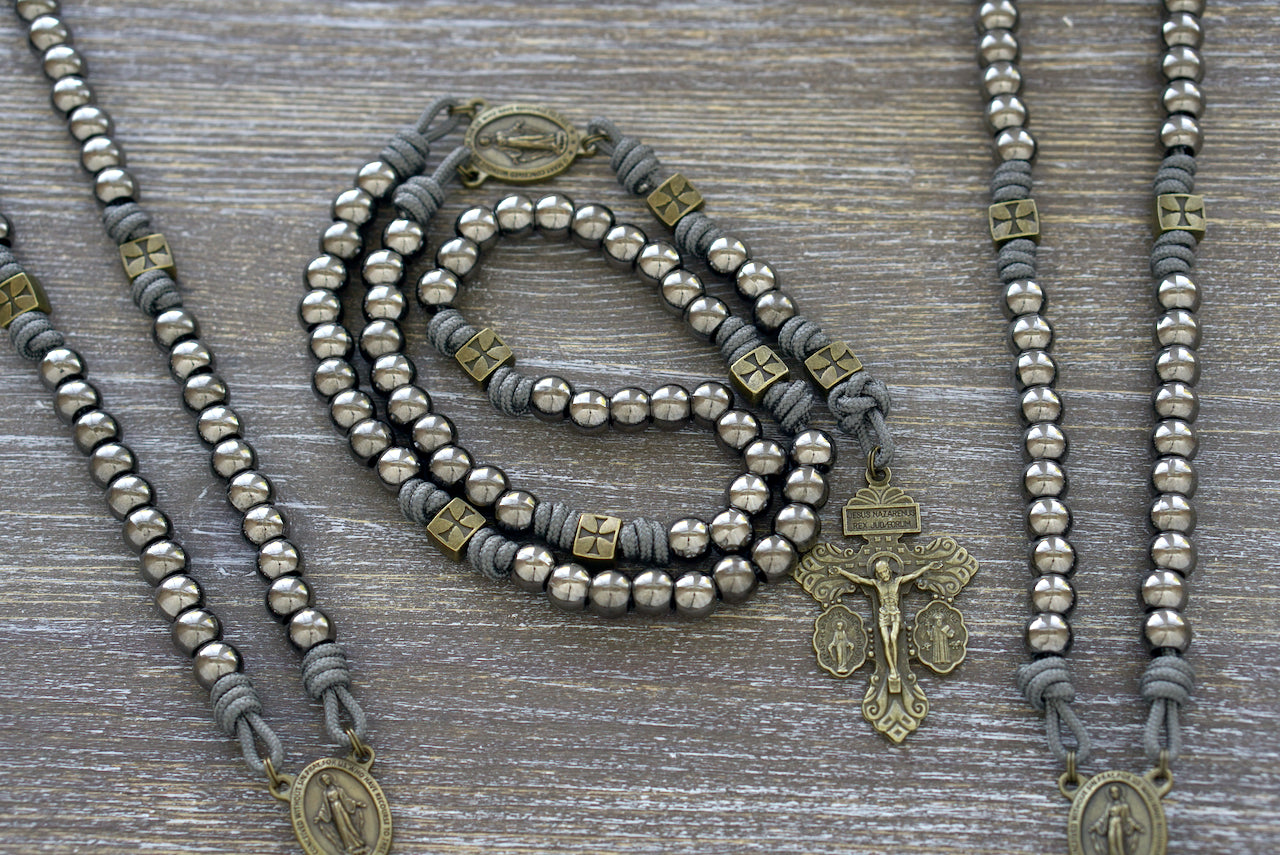 A premium paracord rosary featuring gunmetal & olive metal beads, a Miraculous Medal centerpiece, and a triple threat pardon crucifix. Handcrafted for durability and Catholic devotion.