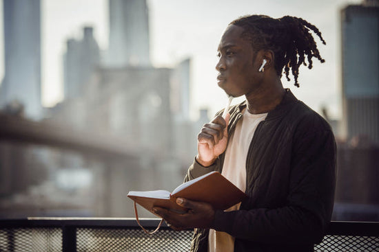 Black man thoughtfully journaling with earbuds