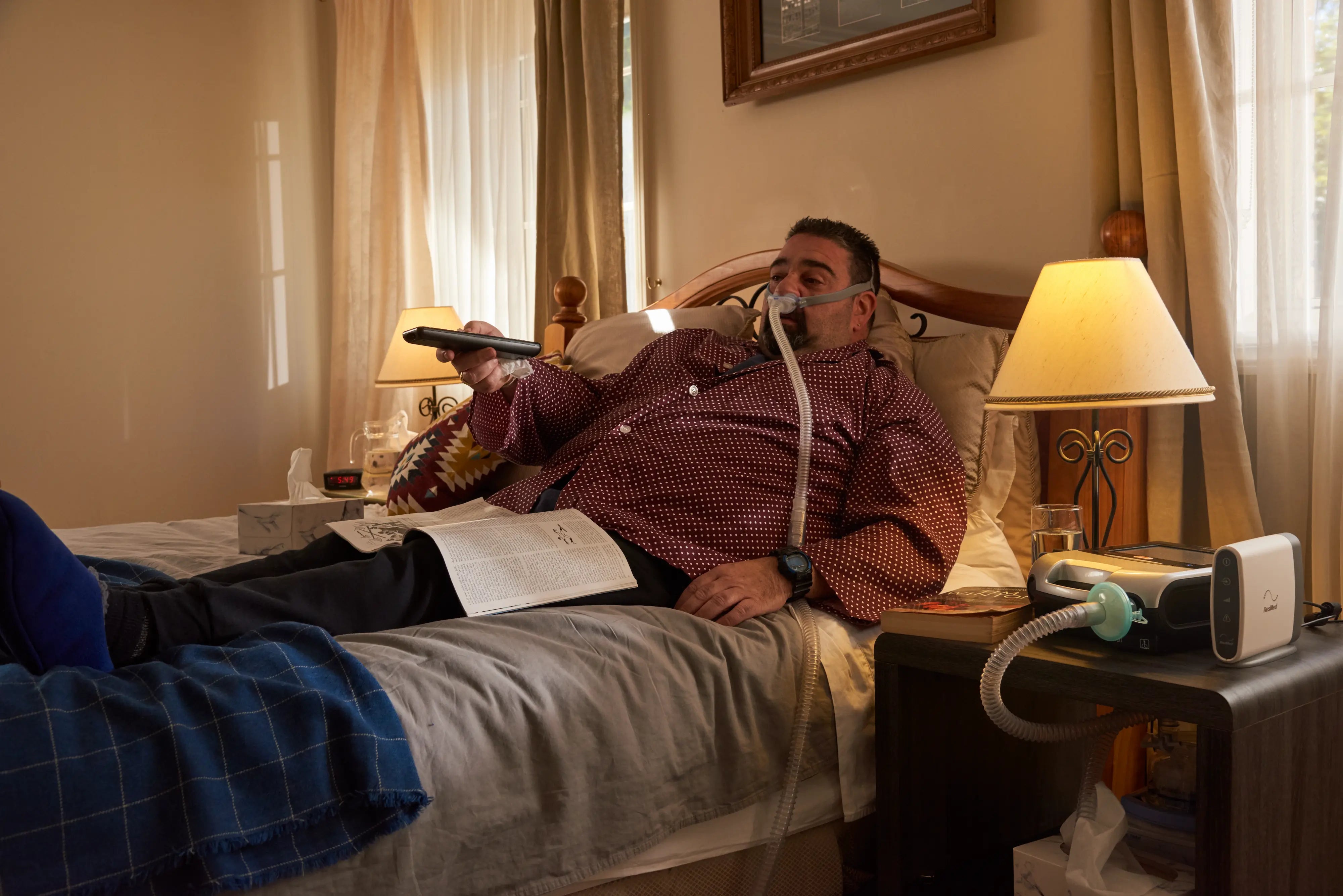 Man in bed holding remote and using cpap machine