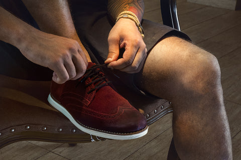 a man tying up his shoes with a brown short and red man shoe