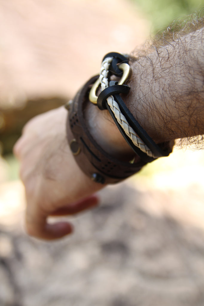a man dressing leather bracelets with a mountain in the background 