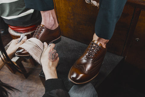 Man wearing a pair of Oxford shoes and receiving a shoeshine.