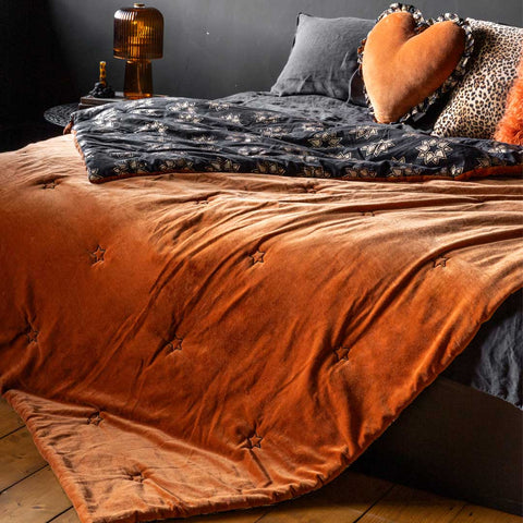 Lifestyle image of the Burnt Orange Reversible Velvet Throw displayed on a bed in a bedroom with other soft furnishings and home accessories.