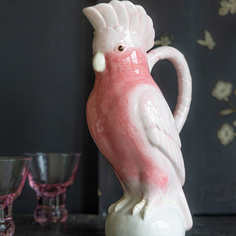 Lifestyle image of the Pink Cockatoo Carafe Jug displayed on a black sidebaord with pink glasses in the background.