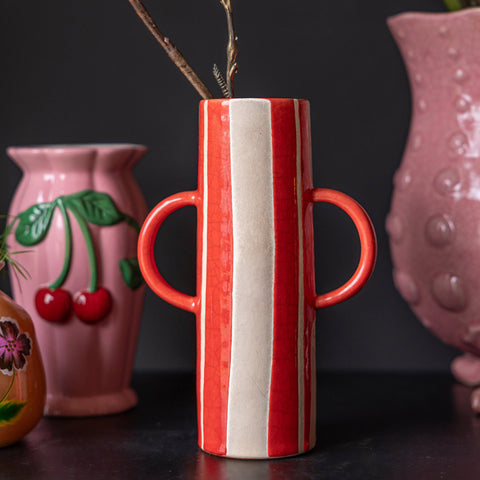 Lifestyle image of the Tall Red Stripe Vase With Handles displayed on a black sideboard with several other Rockett St George vases in the background.