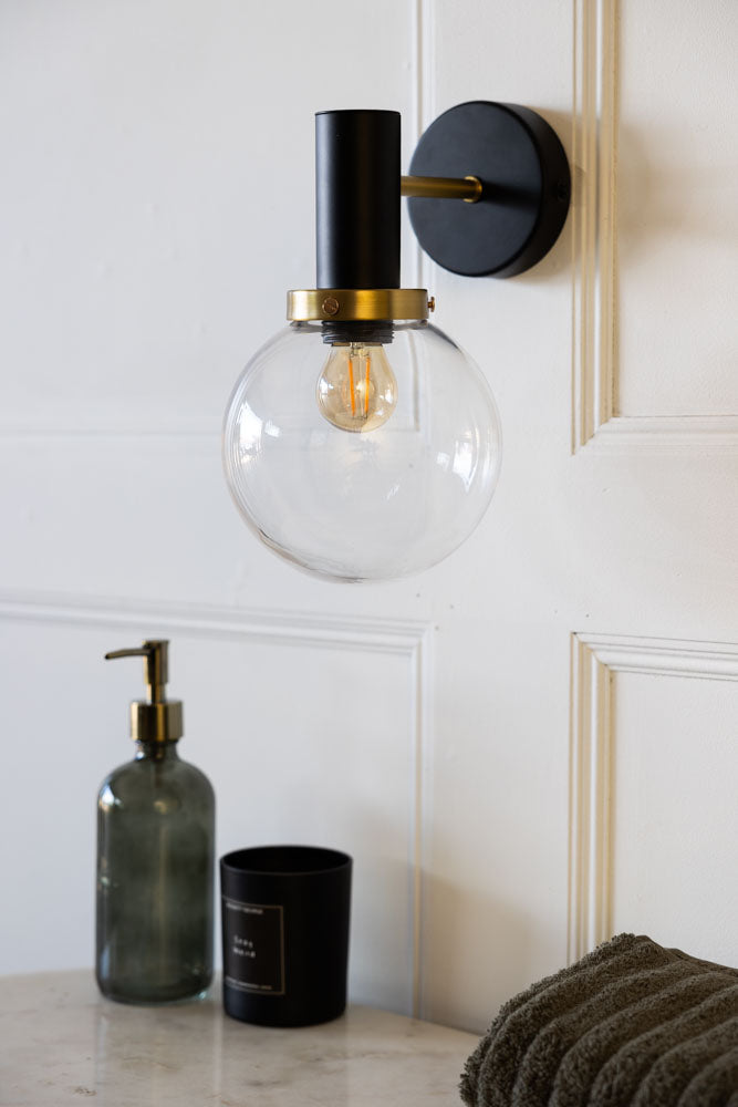 Lifestyle image of the Rockett St George Black & Brass Glass Outdoor Wall Light displayed on the wall of a bathroom and styled with other bathroom accessories.