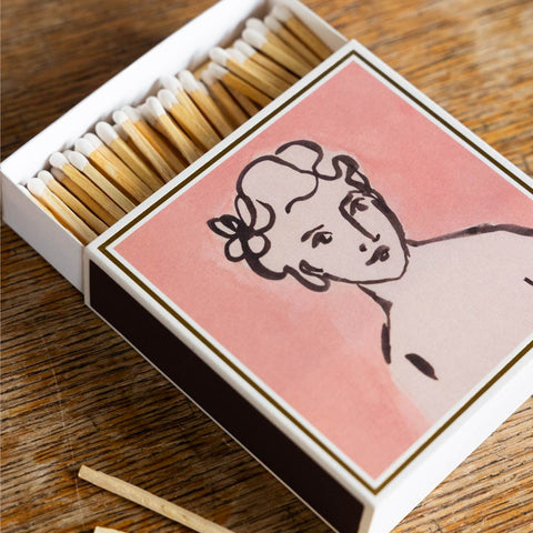 Lifestyle image of the Divine Luxury Matches by Wanderlust Paper Co. open with matches displayed around it on a wooden table.
