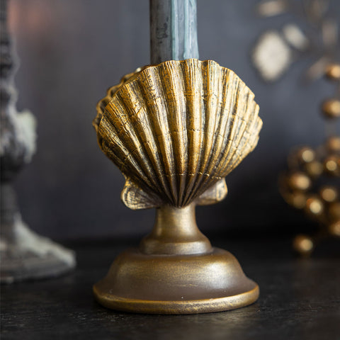 Lifestyle image of the Gold Clam Shell Candlestick Holder displayed on a black sideboard with a candle inside.