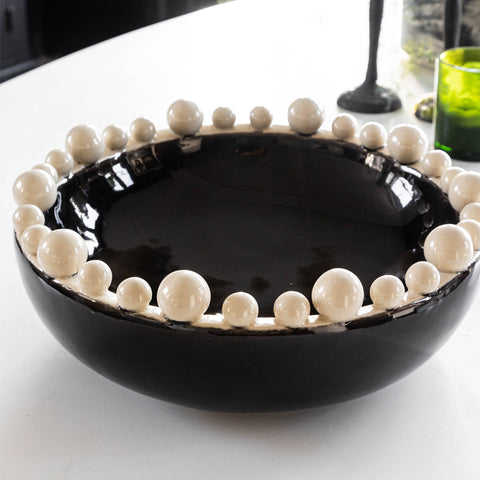 Lifestyle image of the Large Black & Cream Bobble Edged Bowl styled on a table with other home accessories.