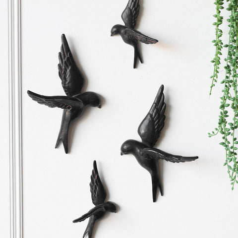 Lifestyle image of the Set Of 4 Black Bird Wall Ornaments displayed on a white wall with some greenery at the side.