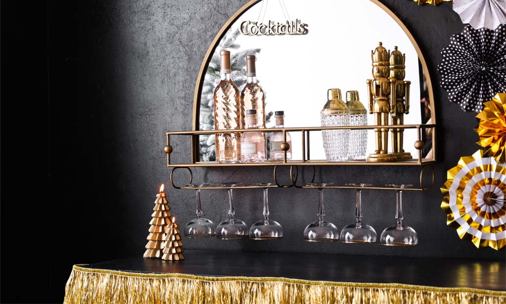 Image of a gold bar shelf mirror adorned with Christmas decorations and glassware.