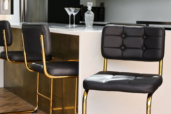 Black faux leather bar stools styled beneath a white and gold kitchen island.