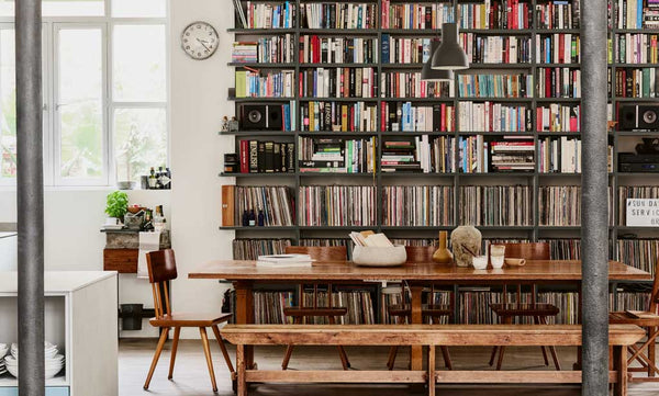 A wooden desk with bench seating in an industrial home against a wall of books.