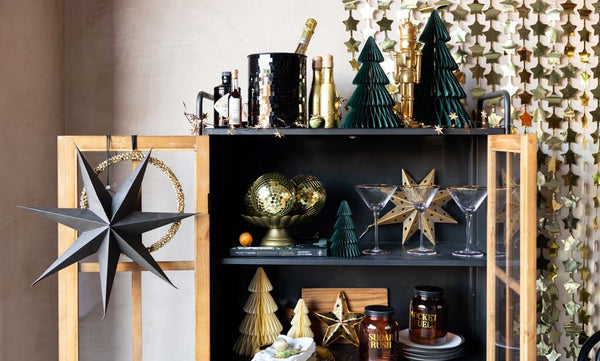 Image of an open display cabinet styled with Rockett St George Christmas decorations including paper stars, honeycomb trees and a gold foil star curtain.