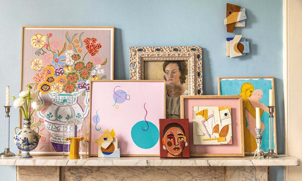 A collection of beautiful and colourful artwork styled on top of a marble fireplace.