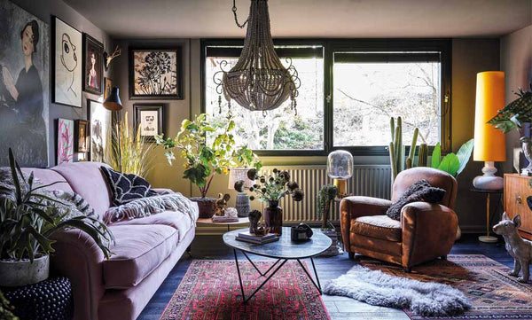 A gorgeous dark living room with a collection of art on the walls, a statement chandelier and cosy vintage rugs.