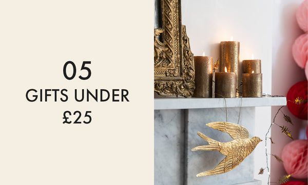 An image of a gold swallow hanging decoration on a grey marble fireplace with gold candles.