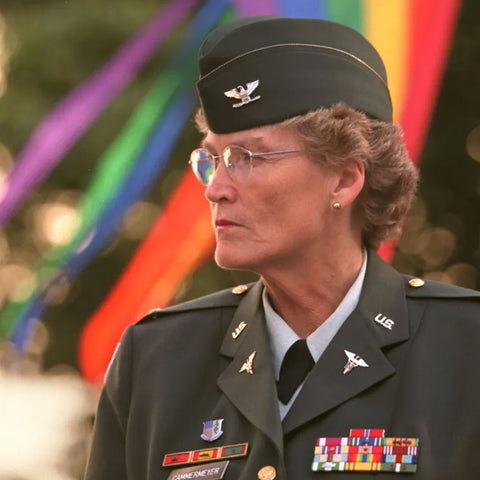 Margarethe Cammermeyer in military uniform. In the background a pride flag is blowing in the wind.