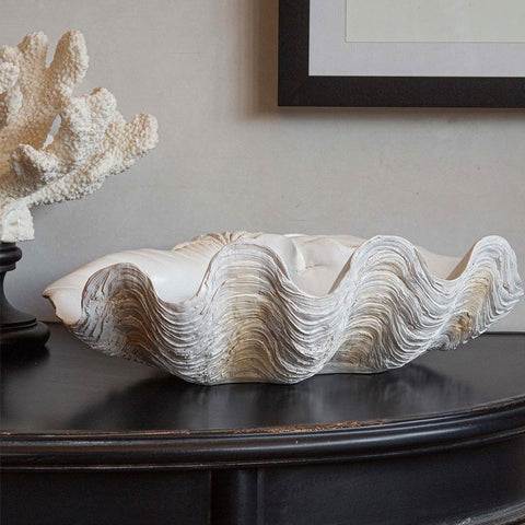 Lifestyle image of the Large White Clam Shell Display Dish displayed on a black table with another ornament and an art print on the wall in the background.