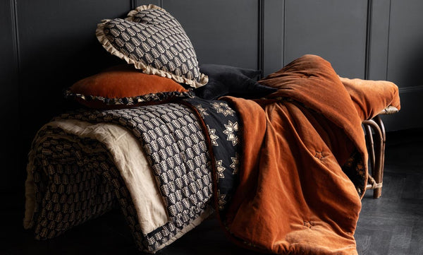 A bench with layers of cushions and throws in velvet and block printed patterns.