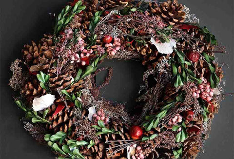 Image of a festive christmas wreath adorned with pinecones, faux berries and ivy.