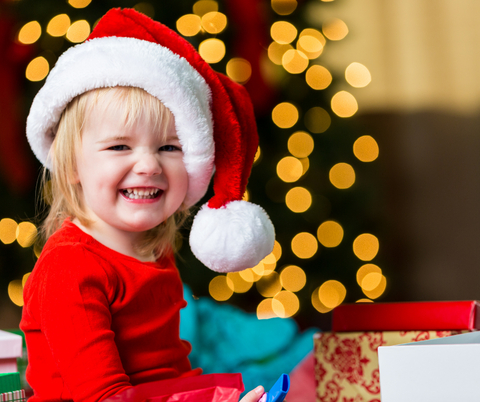 Happy smiling toddler in a Santa hat in front of a sparkly Christmas tree