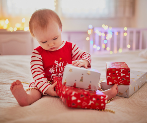 doddl gift guide - baby dressed in red and white plays with Christmas wrapped gifts