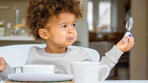 Happy toddler boy sitting at kitchen table at mealtime