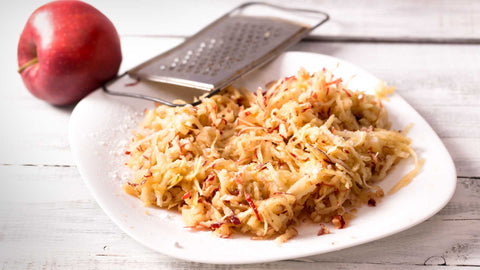 A red apple, a grater and grated apple on a white plate