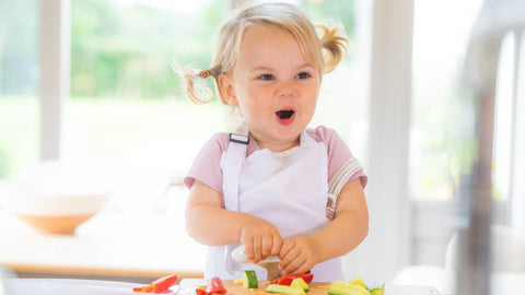 toddler girl chopping vegetables and smiling