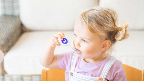 Toddler girl eating with a doddl toddler spoon