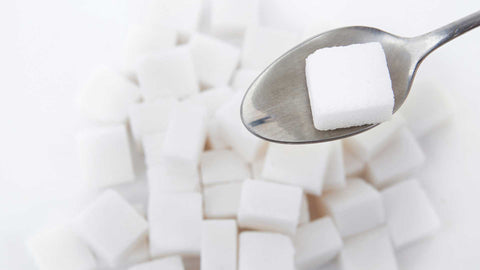 white sugar lumps on a white background, a teaspoon holds one sugar lump