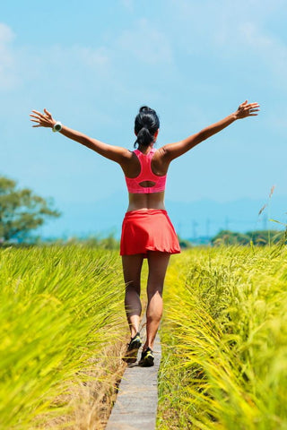 A woman walking in an open field with her arms spread out