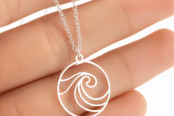 Close-up of a hand holding a Waves of Remembrance Necklace featuring a silver chain and a circular pendant with an elegant wave design