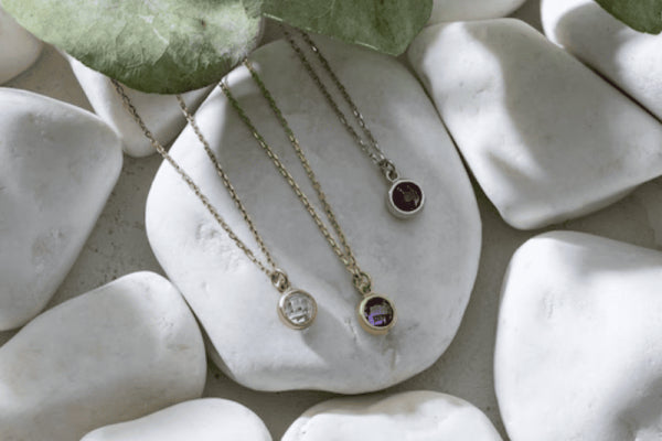 Littlest Spark Birthstone Necklace on white pebbles with elegant colorful birthstone pendants.