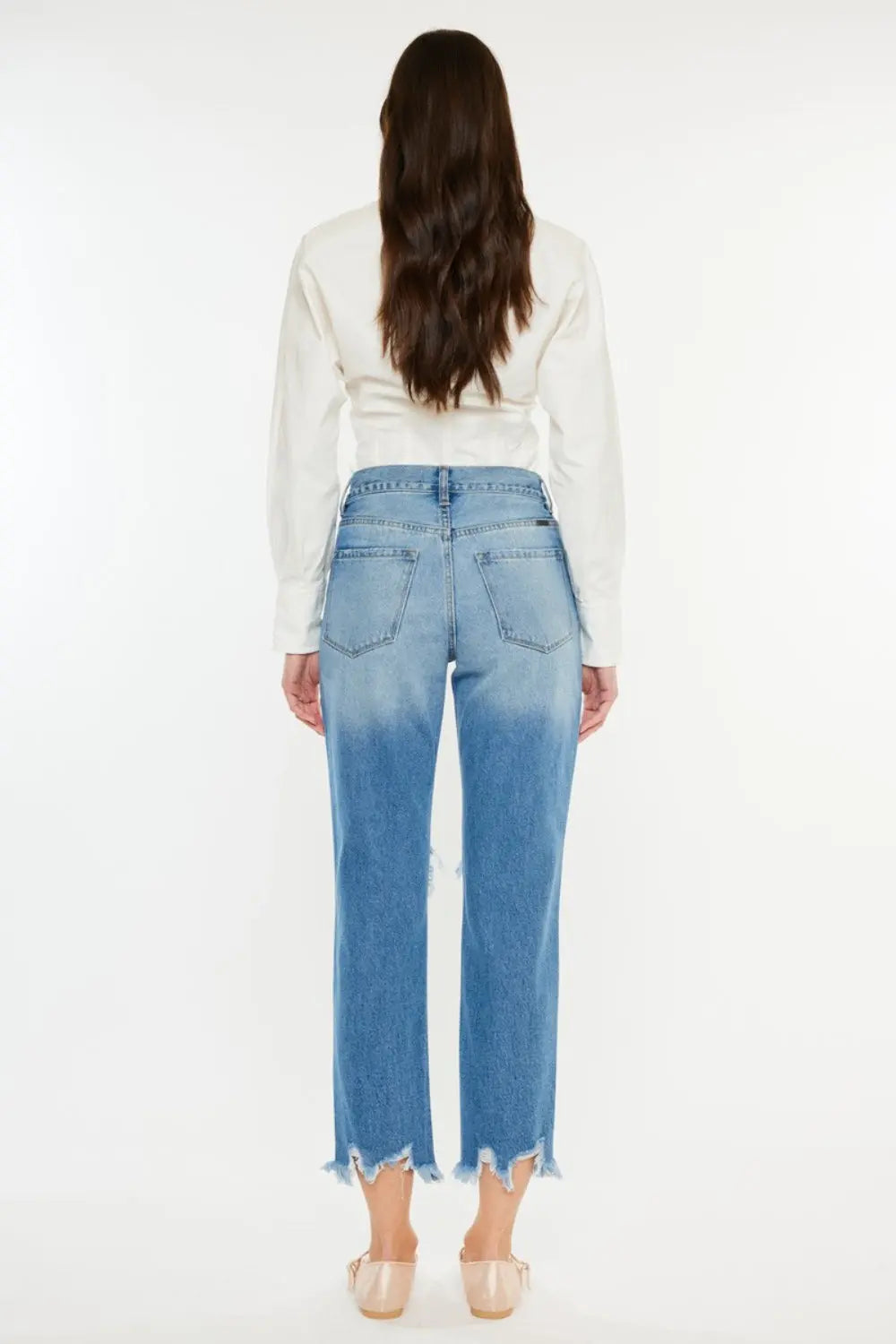 Vista posterior de la modelo con un par de jeans recortados con dobladillo deshilachado y desgastado Kancan.