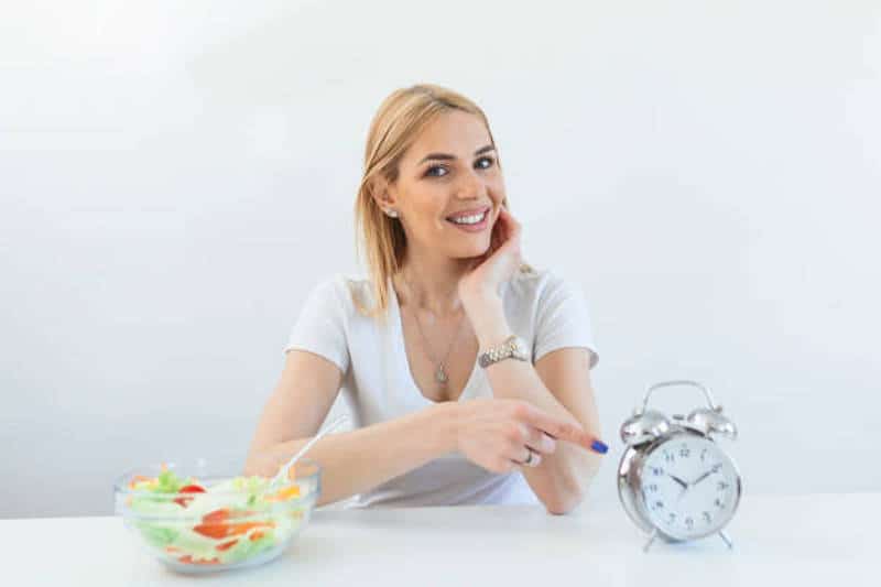 Retro alarm clock in which woman make Intermittent fasting with a Healthy food of salad.