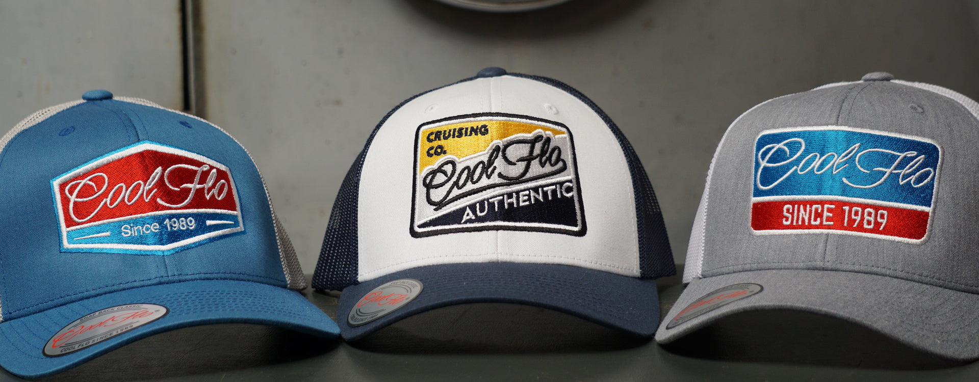 Three Cool Flo embroidered caps positioned in front of a grey VW bus.