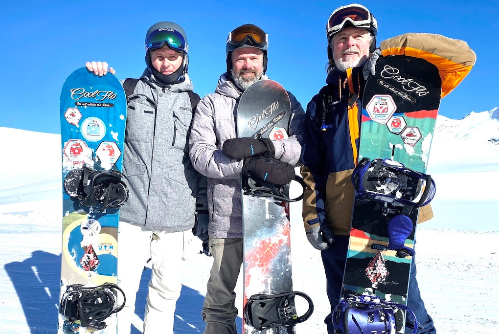 The three Carter Brothers, founders of Cool Flo, on a snowy mountain with their snowboards and a blue sky backdrop.