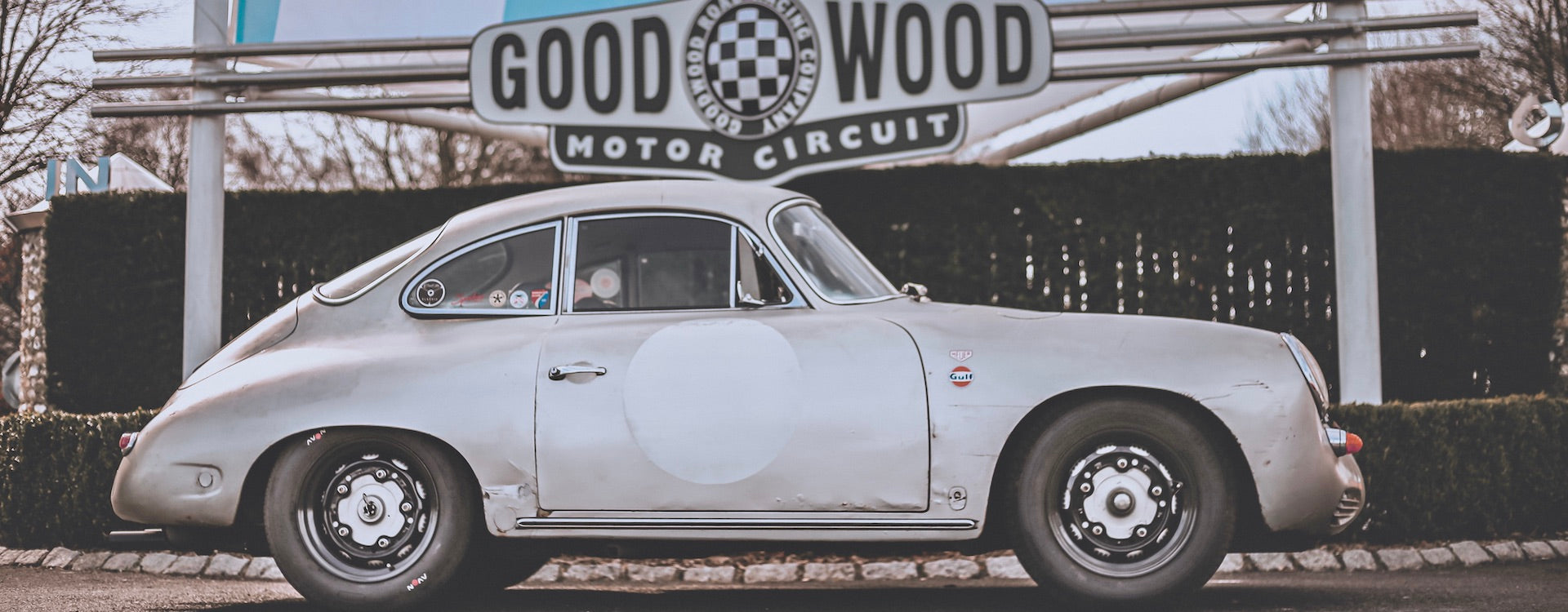 Cool Flo Silver Porsche 356 parked side-on below the Goodwood Motor Circuit sign.
