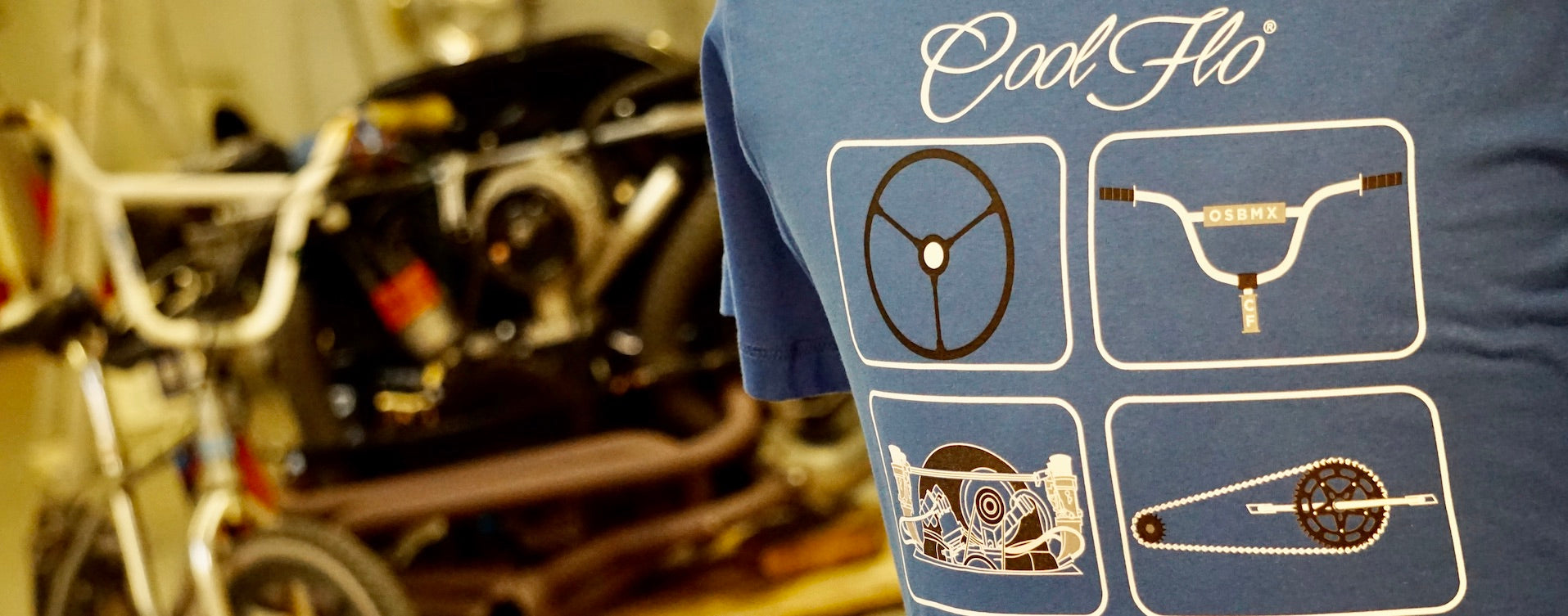 Close-up of a Cool Flo blue BMX and VW design t-shirt in the foreground with a BMX and VW engine out of focus in the background.